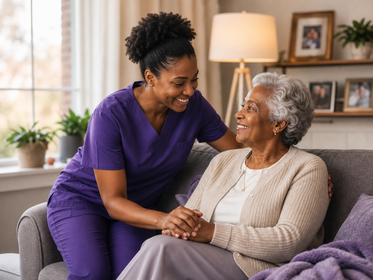 A caregiver and an older woman smiling and holding hands in a bright living room